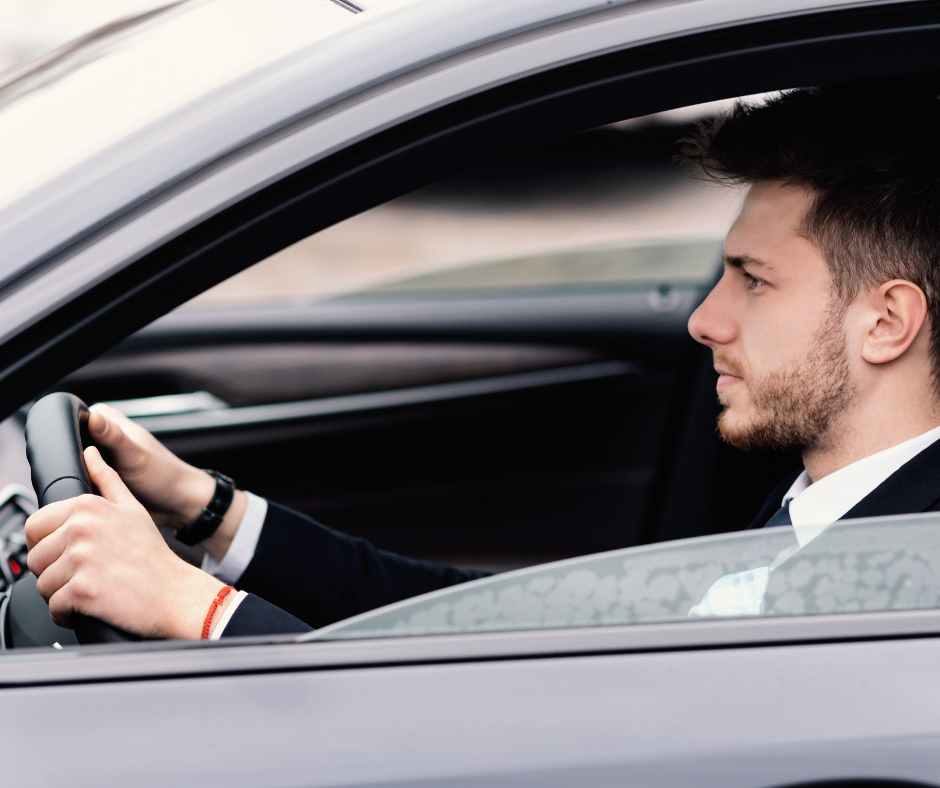 man holding steering wheel of his car while focusing on the road
